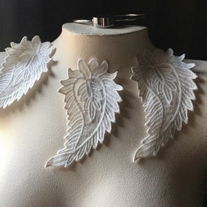 May include: Three white lace appliques in the shape of a feather, displayed on a white mannequin.