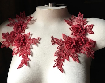 May include: Two red lace appliques with floral designs. The appliques are on a white background and feature delicate floral patterns with raised 3D flowers.