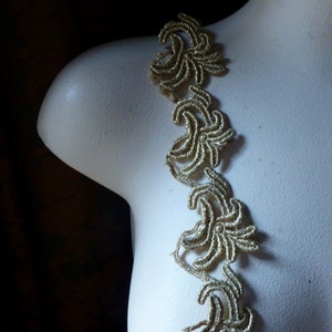 Może przedstawiać: Złota koronka ozdobna z kwiatowym wzorem. Koronka jest delikatna i misterna, z błyszczącym wykończeniem.