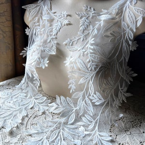 May include: White lace trim with a delicate floral design. The lace features a repeating pattern of leaves and branches.