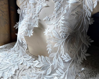 May include: White lace trim with a delicate floral design. The lace features a repeating pattern of leaves and branches.