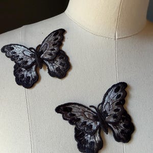 May include: Two embroidered butterfly patches. The butterflies have black outlines and wings with a silver and black pattern. The patches are displayed on a mannequin.