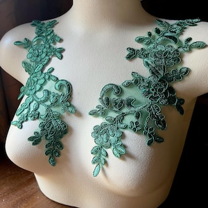 Könnte beinhalten: Zwei smaragdgrüne Spitzenapplikationen mit floralen und Blattmotiven. Die Applikationen werden auf einer Schaufensterpuppe präsentiert, die ihre komplizierten Details und die mögliche Platzierung auf Kleidungsstücken oder Bastelarbeiten zeigt.