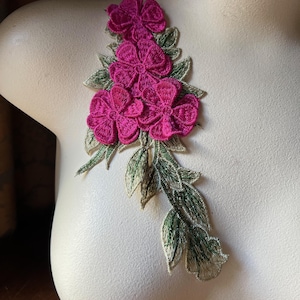 Pode incluir: Uma aplicação floral rosa com folhas verdes. A aplicação é feita de tecido bordado e é perfeita para adicionar um toque de elegância a qualquer projeto.