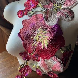 May include: A floral applique with a large red flower, a smaller pink flower, and several smaller red flowers. The applique is made of embroidered fabric and has a vintage style.