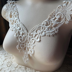 May include: White lace trim with a delicate floral pattern. The trim is shown on a white mannequin bust.