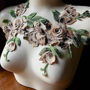 Puede incluir: Una delicada aplicación floral con flores marrones y beige y hojas verdes. La aplicación se muestra en un busto de maniquí blanco.