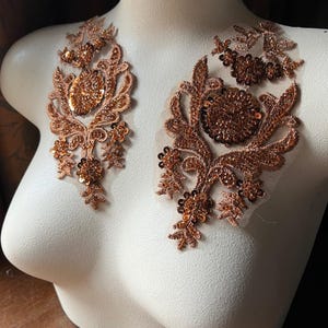 May include: Two copper-colored lace appliques with sequins. The appliques feature a floral design with intricate details.