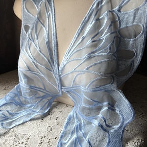 Puede incluir: Aplique de encaje de color azul claro en forma de mariposa con un diseño delicado e intrincado. El encaje es transparente y tiene una textura suave y fluida.