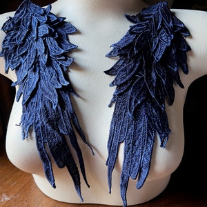 May include: Two navy blue lace appliques shaped like wings, each with a layered design of overlapping leaves. The appliques are displayed on a white mannequin bust.