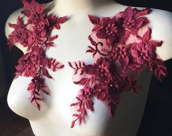 May include: Two burgundy floral lace appliques with pearl accents on a white mannequin.