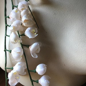 May include: A garland of delicate white silk flowers with green stems. The flowers are arranged in a cascading pattern, creating a romantic and elegant look.