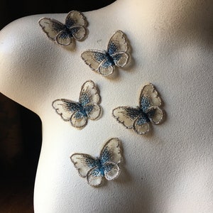 May include: Five sheer, light blue and beige butterfly appliques with embroidered details. The butterflies are arranged on a white surface.
