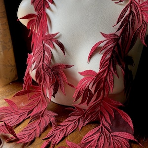 May include: Burgundy red lace trim with a leafy design. The lace is delicate and has a soft, flowing texture.