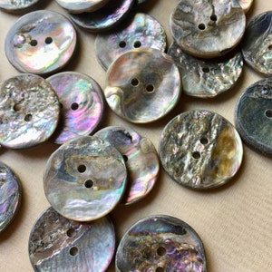 May include: A collection of round, two-hole buttons crafted from iridescent abalone shell. Each button displays a unique, natural pattern with swirling hues of purple, green, blue, and brown, featuring a smooth, polished surface with a distinct pearlescent sheen.