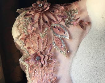 May include: A close-up of a delicate lace fabric with a floral design in shades of pink and gold. The lace features small, sparkling rhinestones.