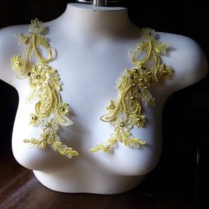 May include: Two yellow floral lace appliques with beaded and sequin accents. The appliques are displayed on a white mannequin torso, showcasing the intricate design and potential for embellishment in fashion or craft projects.