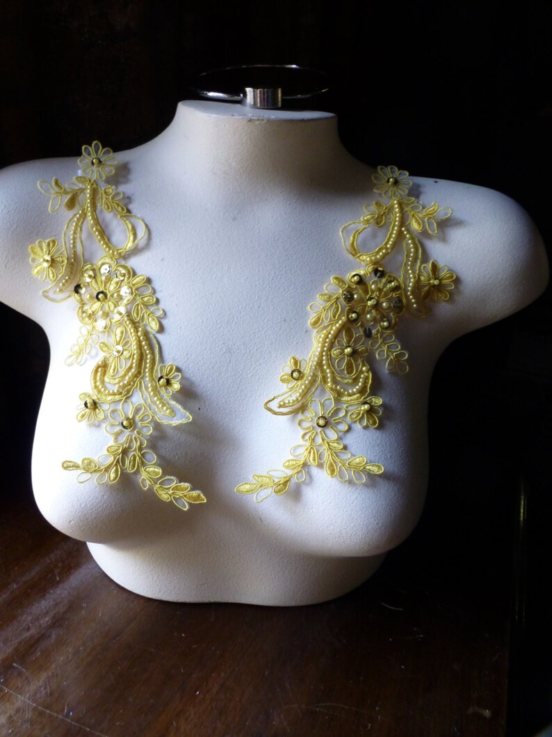 May include: Two yellow floral lace appliques with beaded and sequin accents. The appliques are displayed on a white mannequin torso, showcasing the intricate design and potential for embellishment in fashion or craft projects.