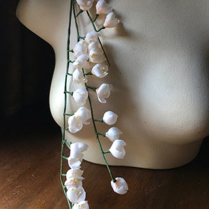 May include: A long strand of white artificial flowers with green stems. The flowers are arranged in clusters along the stems, creating a cascading effect.