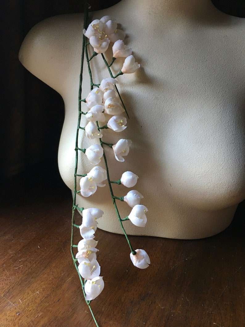 May include: A long strand of white artificial flowers with green stems. The flowers are arranged in clusters along the stems, creating a cascading effect.