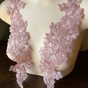 May include: Two pieces of delicate, light pink floral lace applique. The lace features intricate embroidered flowers and leaves, with a sheer mesh backing. The appliques are displayed on a mannequin, showcasing their potential for garment embellishment.