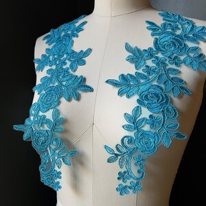 May include: Two turquoise floral lace appliques. Each applique features embroidered roses, leaves, and small flowers. The appliques are displayed on a mannequin, showcasing their design and potential use in garment decoration.
