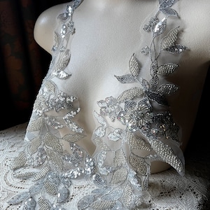 May include: Silver sequined floral applique with a delicate mesh backing. The applique features a vine design with leaves and flowers.