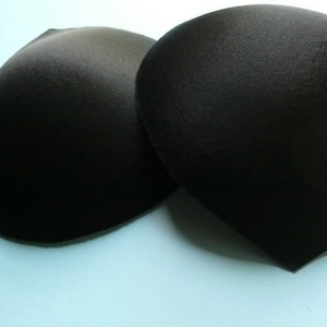 May include: Two black bra cups made of foam padding. The cups are curved and have a smooth surface.