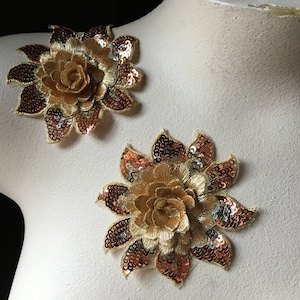 Pode incluir: Dois apliques de flores de lantejoulas douradas e cobre. Cada aplique apresenta um design de flor 3D com uma rosa no centro.