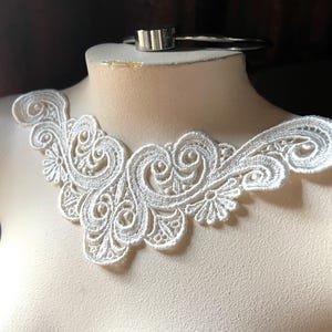 May include: A white lace collar with an intricate floral and swirl design. The collar is displayed on a mannequin, showcasing its delicate details and openwork pattern. The lace is a bright white color.