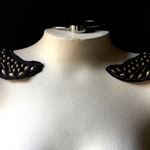 May include: A pair of black fabric shoulder pieces with gold and silver embellishments and dangling chains.