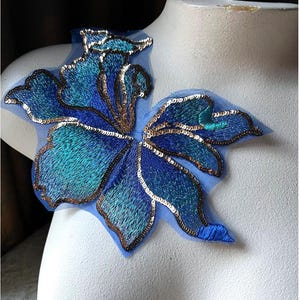 May include: A blue and gold sequined flower applique with a sheer mesh backing. The applique is perfect for adding a touch of sparkle to clothing, bags, or home decor projects.
