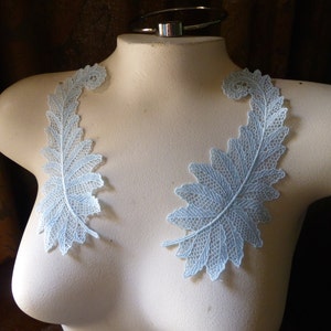 May include: Two light blue lace appliques in the shape of fern leaves. The appliques are on a white mannequin bust.