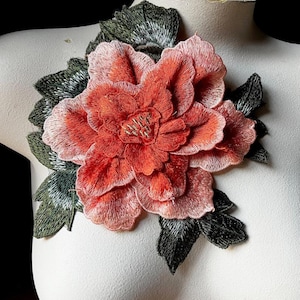May include: A large, pink and orange embroidered flower with green leaves. The flower is detailed and has a 3D effect.