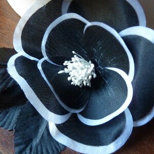 May include: A black fabric flower with white trim and a white center. The flower is layered and has a ruffled appearance.