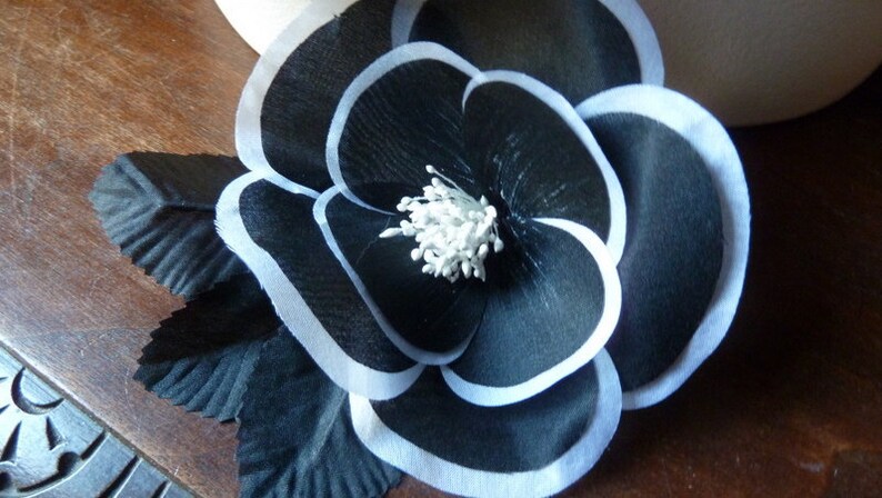 May include: A black fabric flower with white trim and a white center. The flower is layered and has a ruffled appearance.
