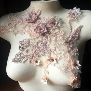 May include: A delicate floral lace applique with pink and brown flowers and beads. The applique is on a white mannequin bust.