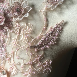 May include: A delicate lace applique with pink and gold embellishments. The applique features floral designs with beaded accents and sequins.