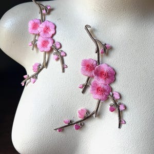 Puede incluir: Diseño de rama floral rosa bordada. Las ramas son marrones con flores y capullos rosas. El diseño se muestra en un maniquí.