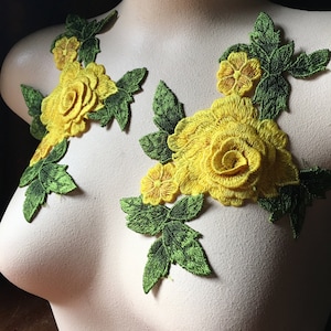 May include: Two yellow rose appliques with green leaves are displayed on a mannequin. The floral embroidery features detailed petals and leaves, creating a three-dimensional effect. The bright yellow roses contrast with the green leaves.