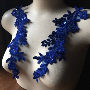 Peut inclure: Deux appliques en dentelle bleu royal avec des paillettes, chacune présentant un motif floral avec des feuilles et des fleurs. Les appliques sont présentées sur un mannequin blanc.