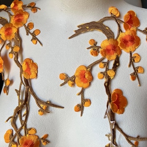May include: Embroidered floral appliques featuring orange and yellow blossoms with brown stems and buds. The appliques are designed to be sewn onto fabric, adding a decorative touch to clothing or crafts.