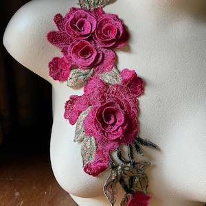 Puede incluir: Una aplicación floral rosa con tres rosas y hojas verdes. La aplicación está hecha de tela y tiene un aspecto delicado y femenino.