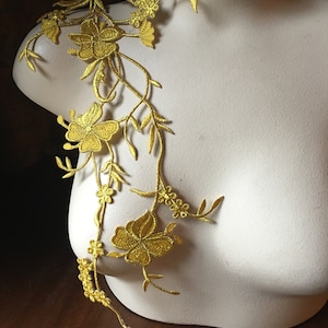 Könnte beinhalten: Ein goldener floraler Spitzenbesatz mit zarten Blüten und Blättern. Der Besatz ist auf einer weißen Schaufensterpuppe zu sehen.