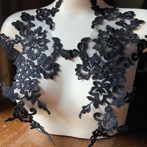May include: Black lace applique with floral designs. The lace is delicate and intricate, with a soft, flowing texture. It is perfect for adding a touch of elegance to any project.