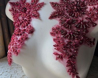 May include: Two burgundy beaded floral appliques on a white mannequin. The appliques are made of burgundy beads and sequins, and they are attached to a sheer fabric.