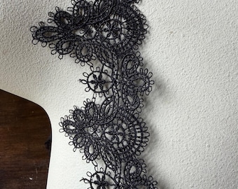 Puede incluir: Un borde de encaje negro que presenta un intrincado patrón floral y circular con bordes festoneados. El delicado trabajo de aguja crea un borde decorativo continuo con detalles calados, mostrando una fina construcción de hilo en toda la pieza.