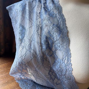 May include: A piece of light blue lace fabric with a floral pattern. The lace has a scalloped edge.