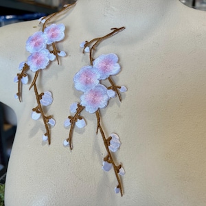 May include: Two embroidered white and pink flower branches with brown stems. The flowers are arranged in a delicate pattern, resembling cherry blossoms.