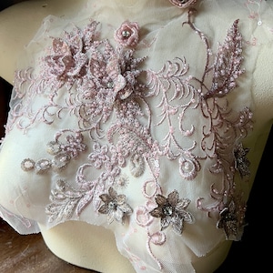 May include: Pink and brown floral lace applique with beaded details. The applique is on a sheer white mesh fabric.